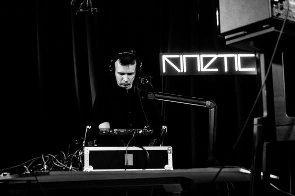 A performer in headphones under the KINETIC neon